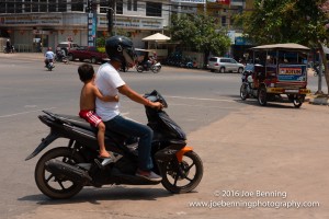A small boy clinging to the driver of a motorbike in Cambodia