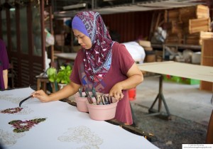 Photo of a woman painting in a stencil in a Batik factory in Penang, Malaysia