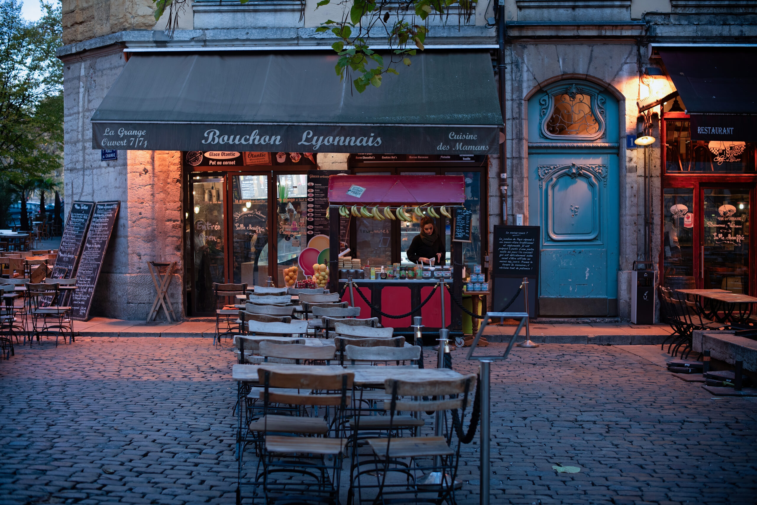 Traditional French bouchon restaurant storefront lit up at dusk in Lyon, France