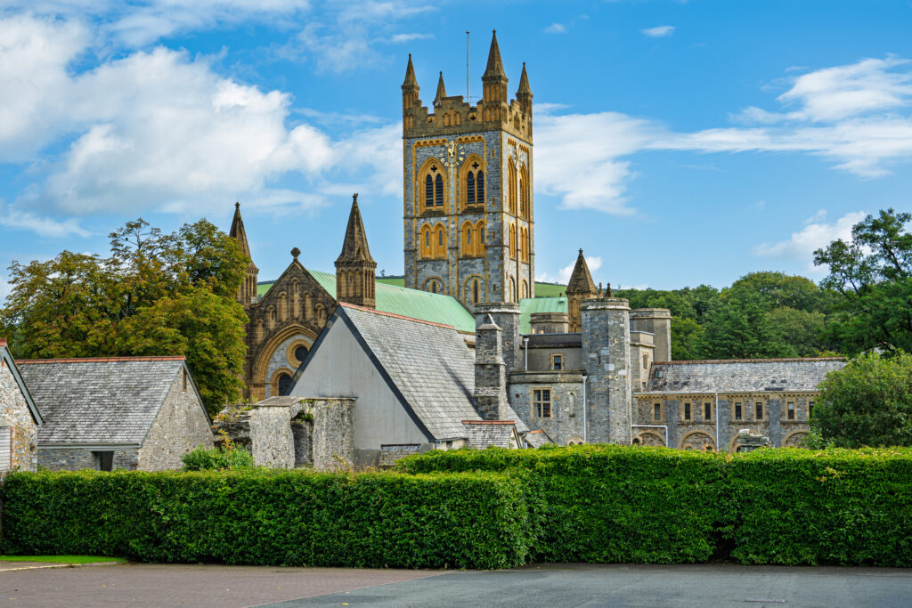 Buckfast Abbey church tower and stone buildings above green hedges in Buckfastleigh, Devon, England.