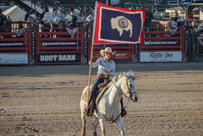 Cowgirl On White Horse Carries Wyoming State Flag At Rodeo