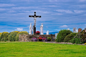 Calvary crucifix with white religious statues, colorful flowers and gravestones in a carefully maintained cemetery in rural Ireland.