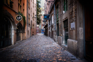 Empty cobblestone side street in Vieux Lyon, France at dusk with scattered autumn leaves