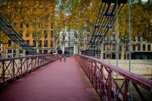 People walking across a red pedestrian footbridge over the Sa&ocirc;ne River in Lyon in autumn