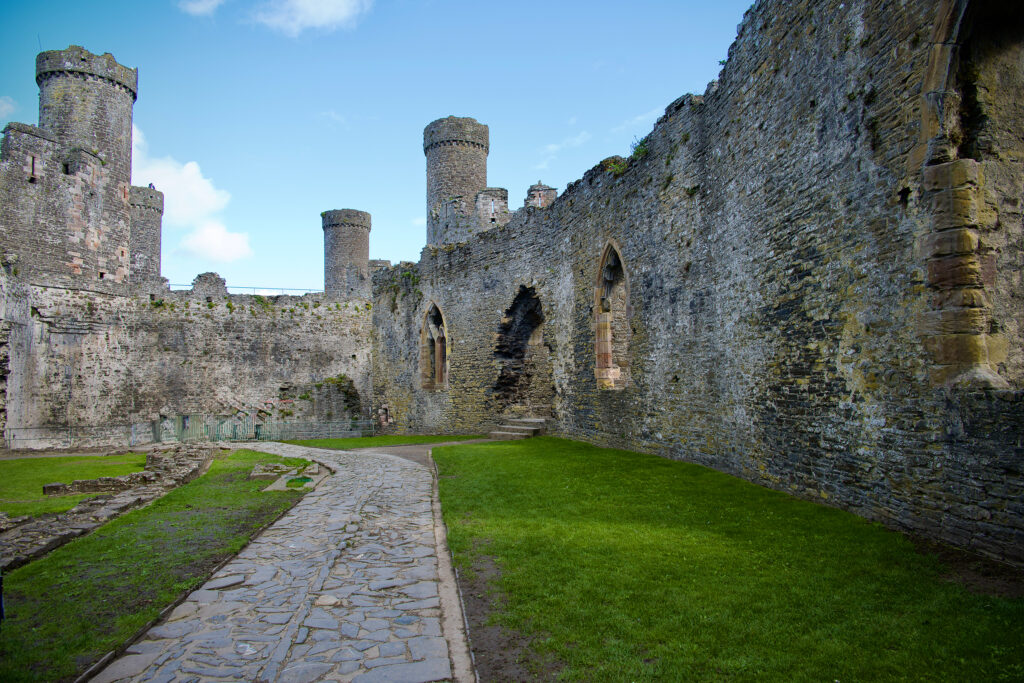 Stone path and green lawn beneath the medieval walls and round towers of Conwy Castle in Wales.