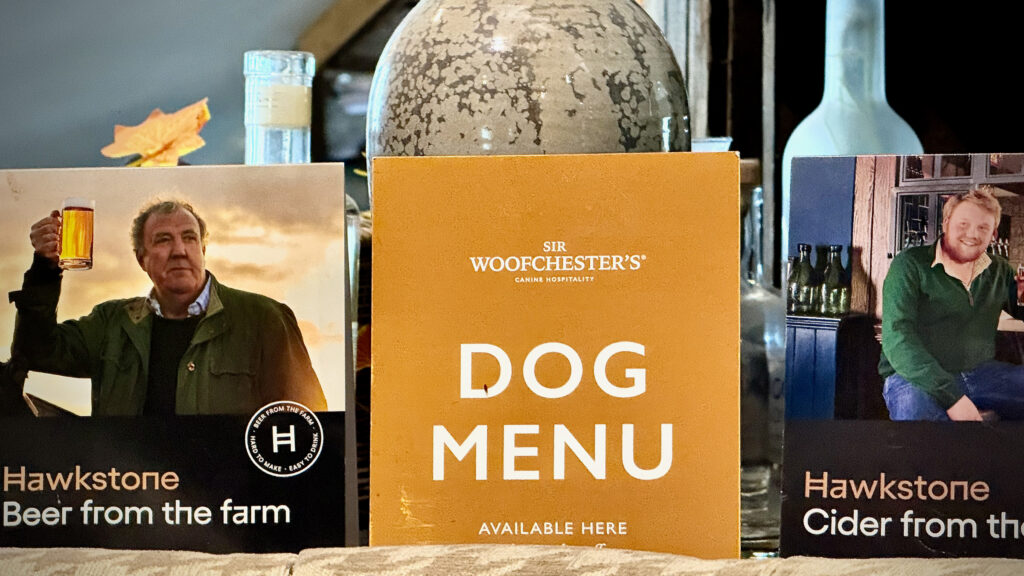 Orange Sir Woofchester’s dog menu between Hawkstone beer and cider promotional signs on a counter.