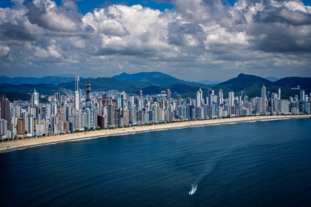 A dense line of waterfront towers borders the beach at Balneário Camboriú beneath dramatic clouds.