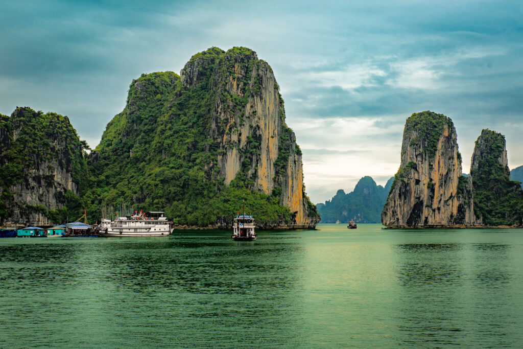 Boats cross green water beneath towering limestone karsts in Ha Long Bay, Vietnam