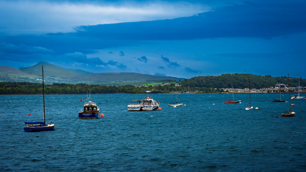 Sailing boats and excursion vessels float off Beaumaris with the mainland hills beyond.