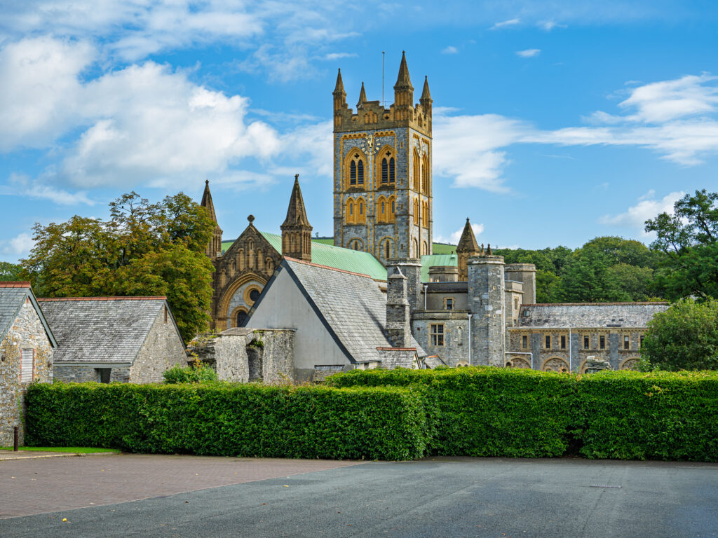 Buckfast Abbey church tower and stone buildings above green hedges in Buckfastleigh, Devon, England.