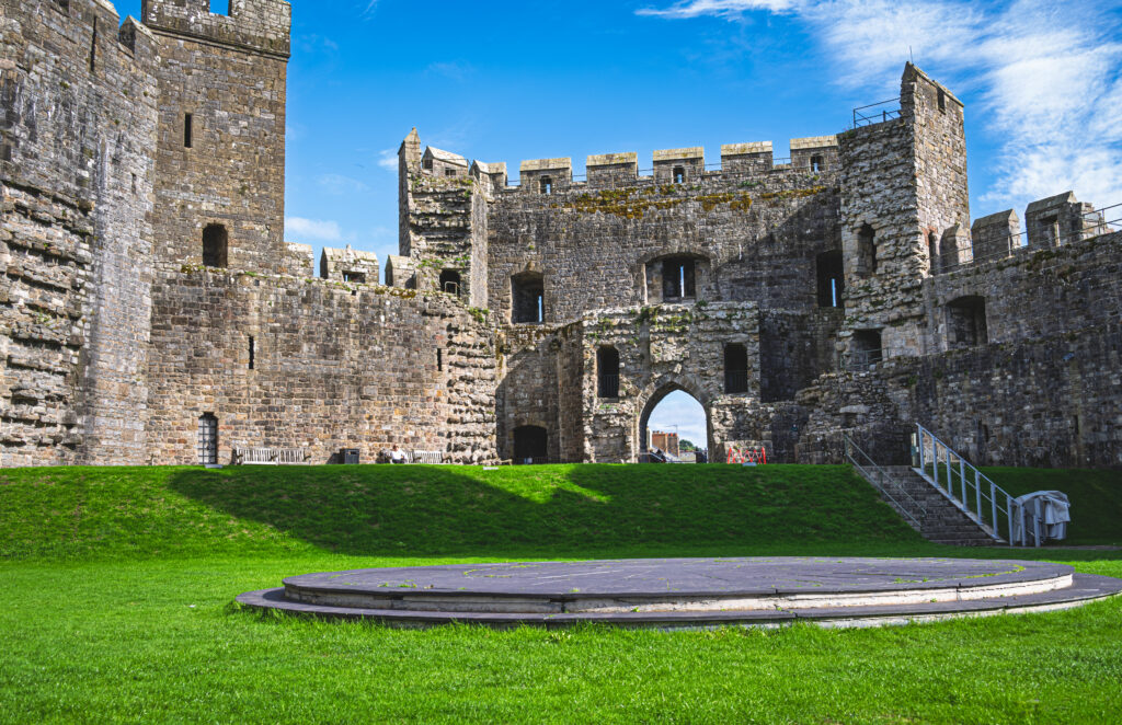A circular slate dais lies on grass inside Caernarfon Castle beneath stone towers and battlements.