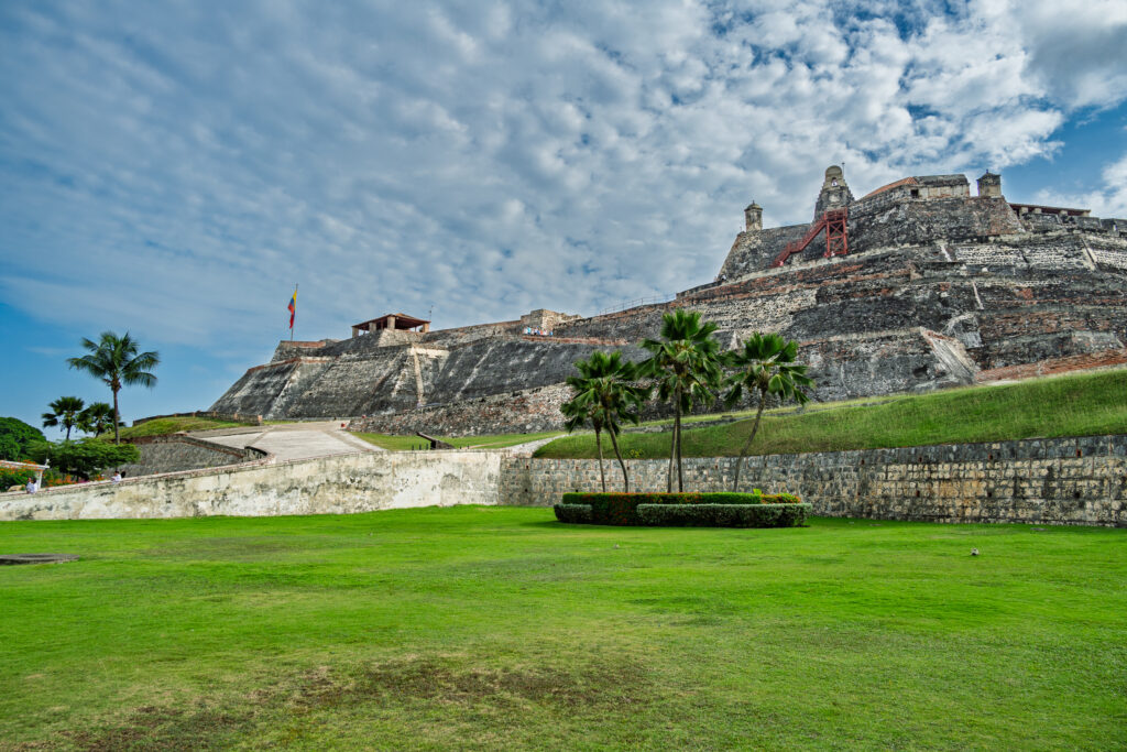 Stone ramparts of Castillo San Felipe de Barajas above a green lawn in Cartagena beneath a cloudy sky.