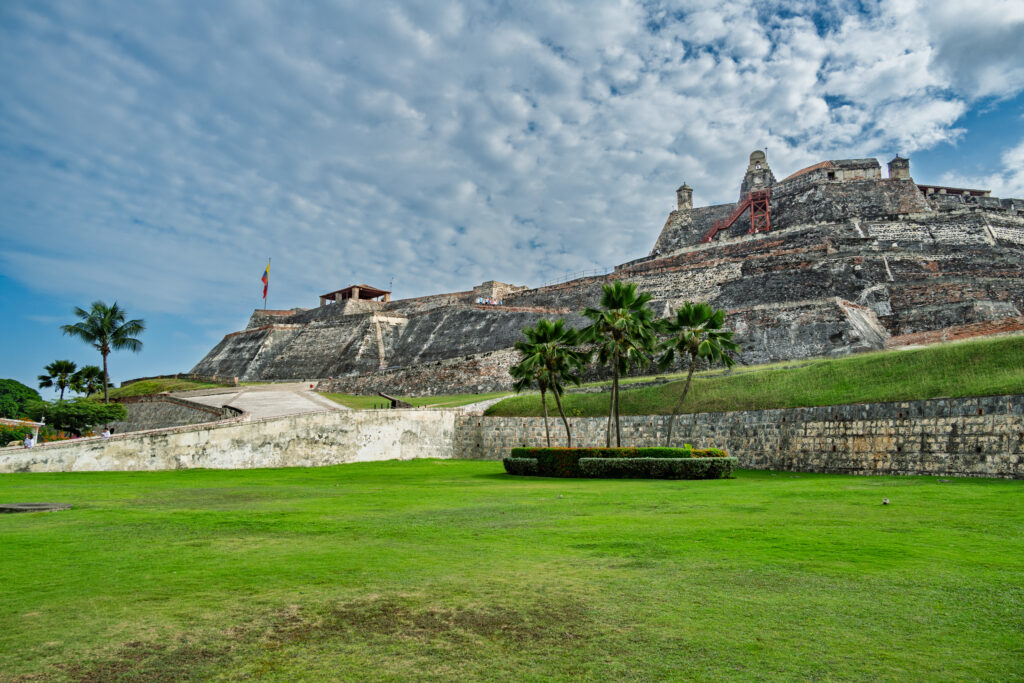 Stone ramparts of Castillo San Felipe de Barajas above a green lawn in Cartagena beneath a cloudy sky.