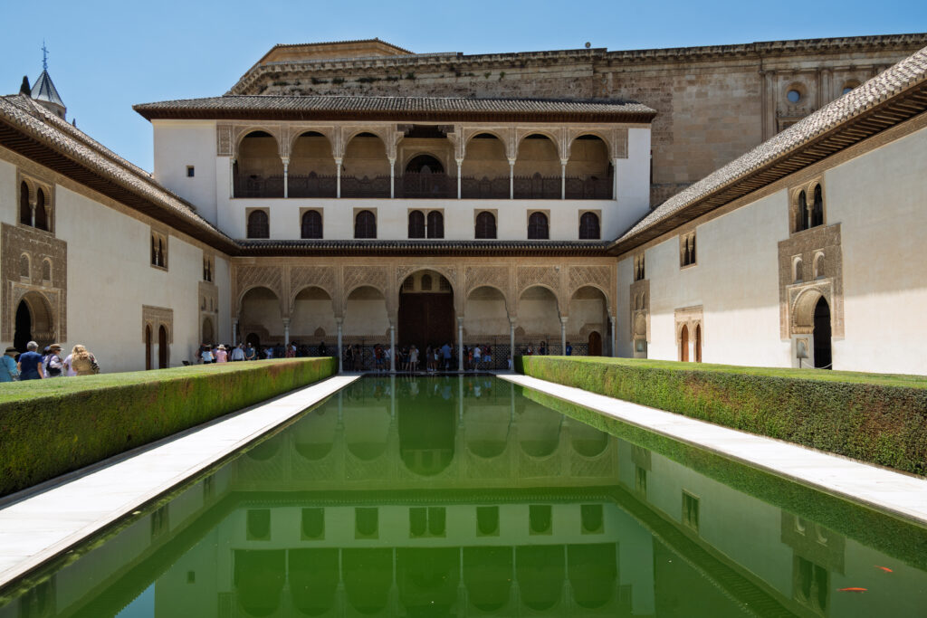 The Alhambra courtyard pool mirrors the palace facade beneath a clear blue sky in Granada.