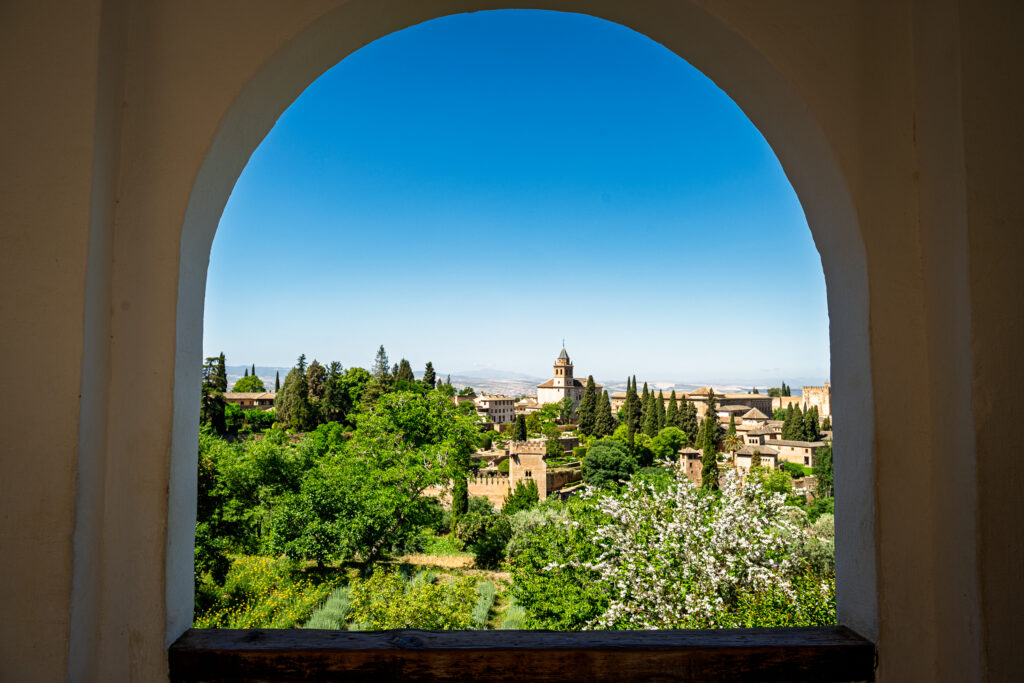 An arch at the Alhambra frames a view across Granada with trees and a distant tower.