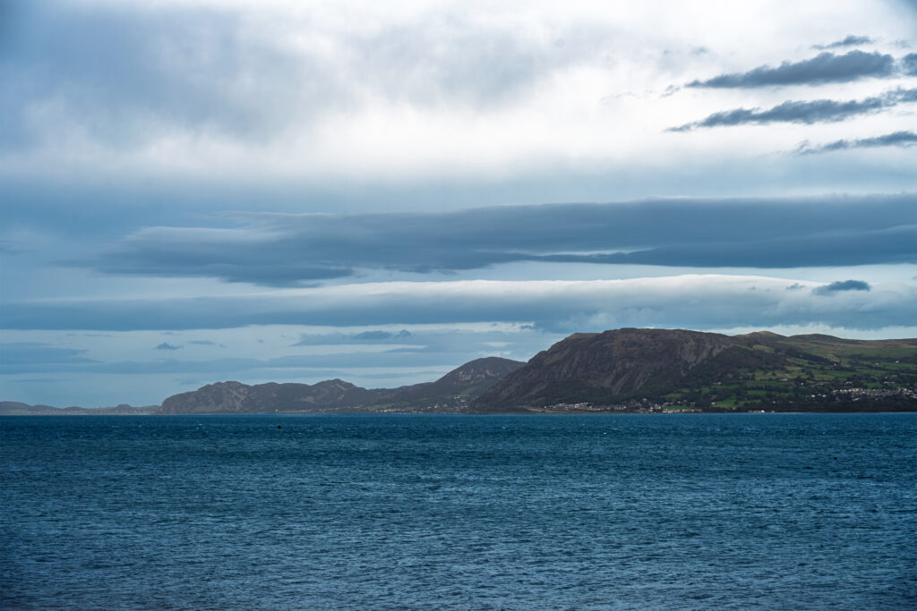 Blue water lies beneath layered grey clouds, with a rugged coastline on the horizon.