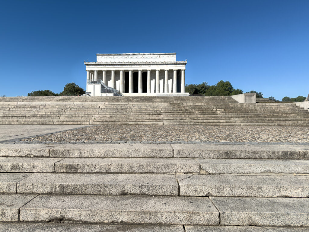 Broad stone steps lead to the columned Lincoln Memorial beneath a clear blue sky in Washington, DC.