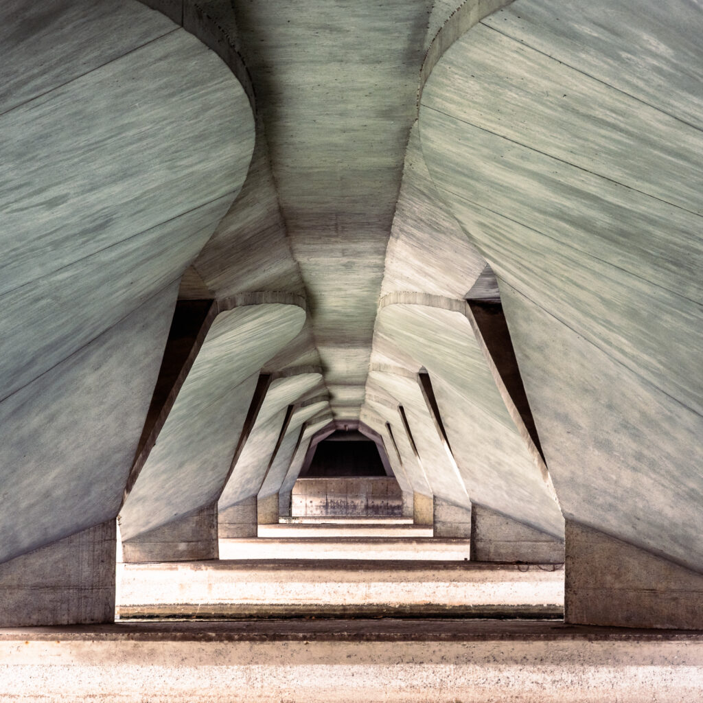 Repeating angular concrete supports frame a dark central opening in a symmetrical architectural view.