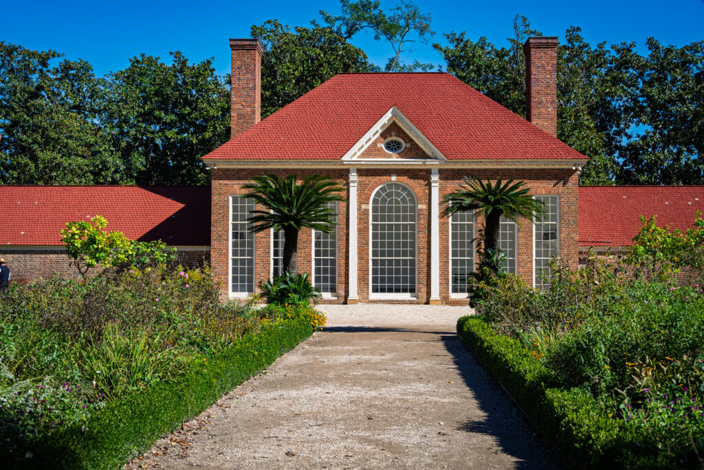 Red brick greenhouse with a red roof and tall arched windows at the end of a garden path at Mount Vernon.