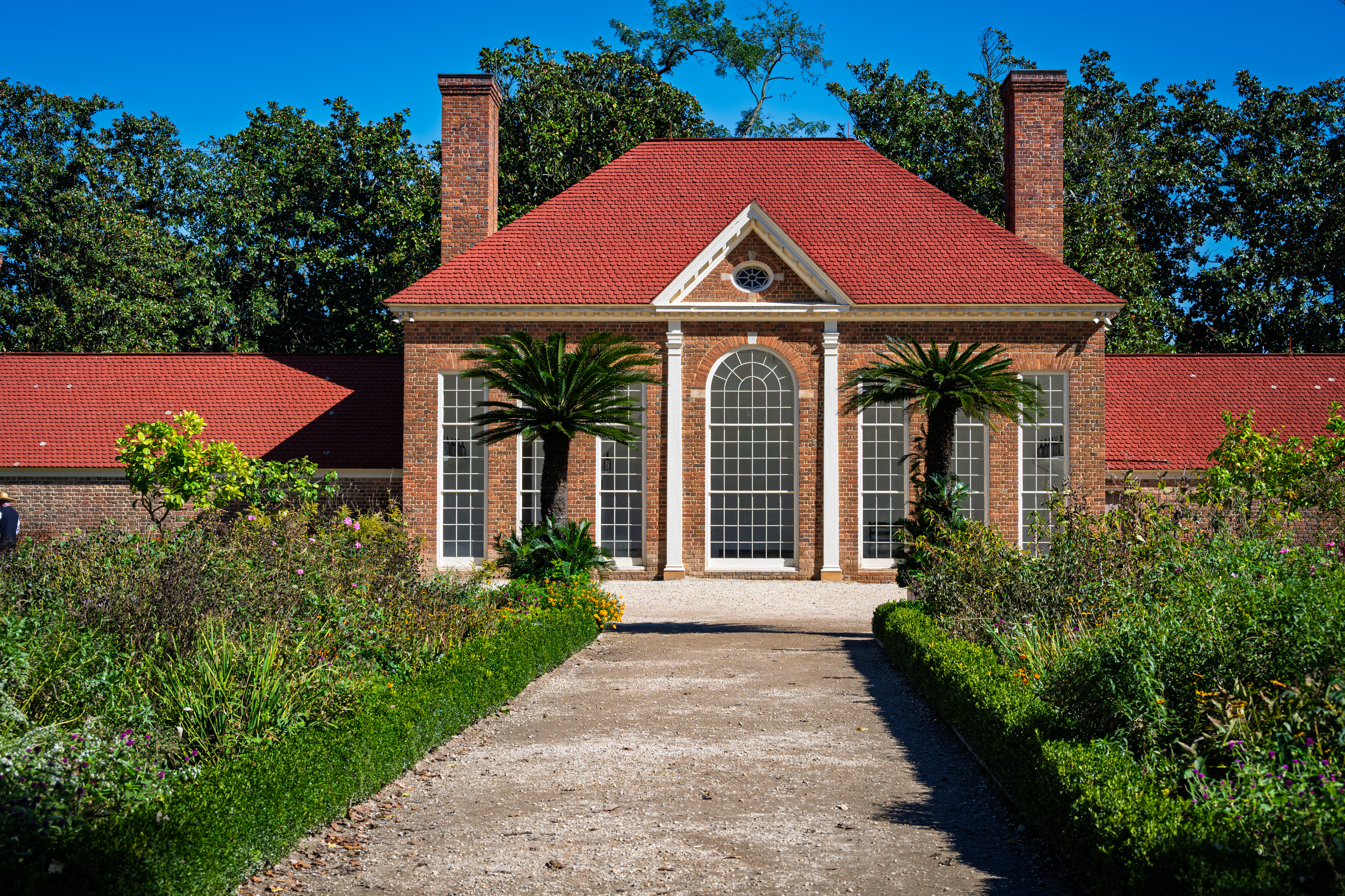 Red brick greenhouse with a red roof and tall arched windows at the end of a garden path at Mount Vernon.