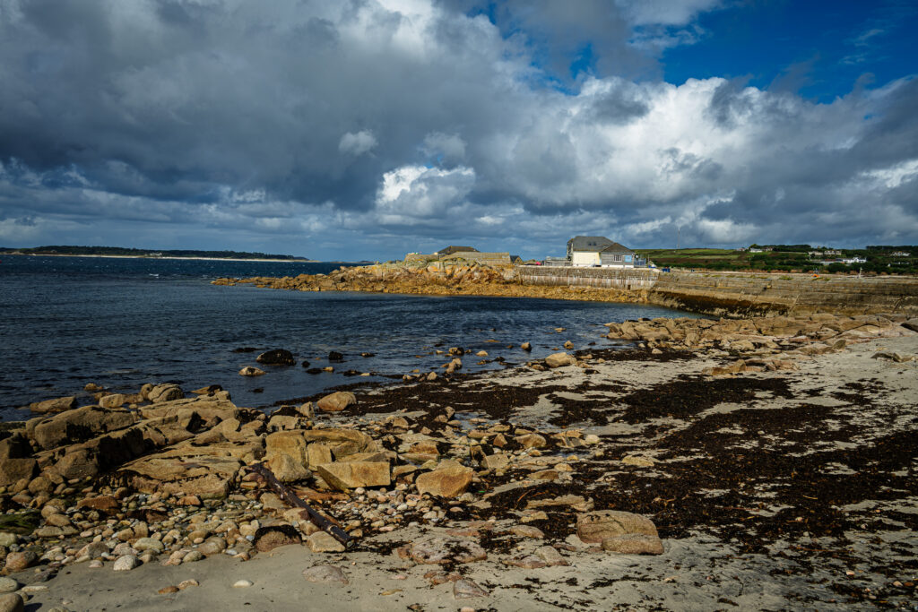 Rocky coastline and calm inlet beneath dramatic storm clouds in the Isles of Scilly, England.