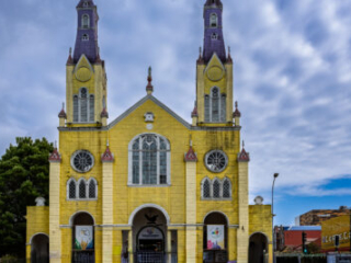 The yellow facade and twin towers of San Francisco Church stand beneath a cloudy sky in Castro, Chile.