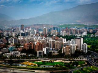 Elevated Santiago skyline with green parkland, curved roads and hazy Andes mountains.