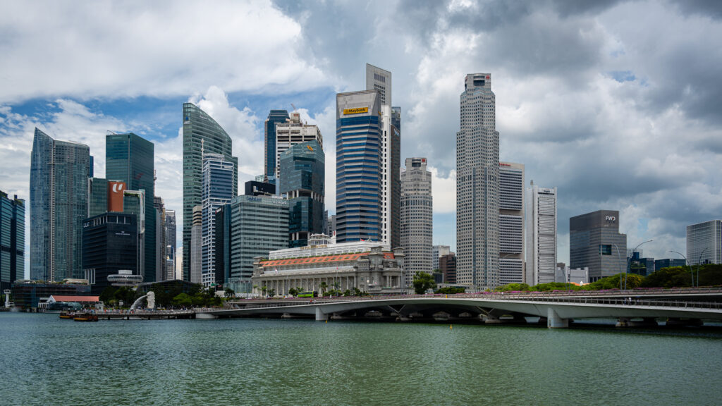 Singapore skyscrapers rise above the waterfront and a low bridge beneath heavy clouds.