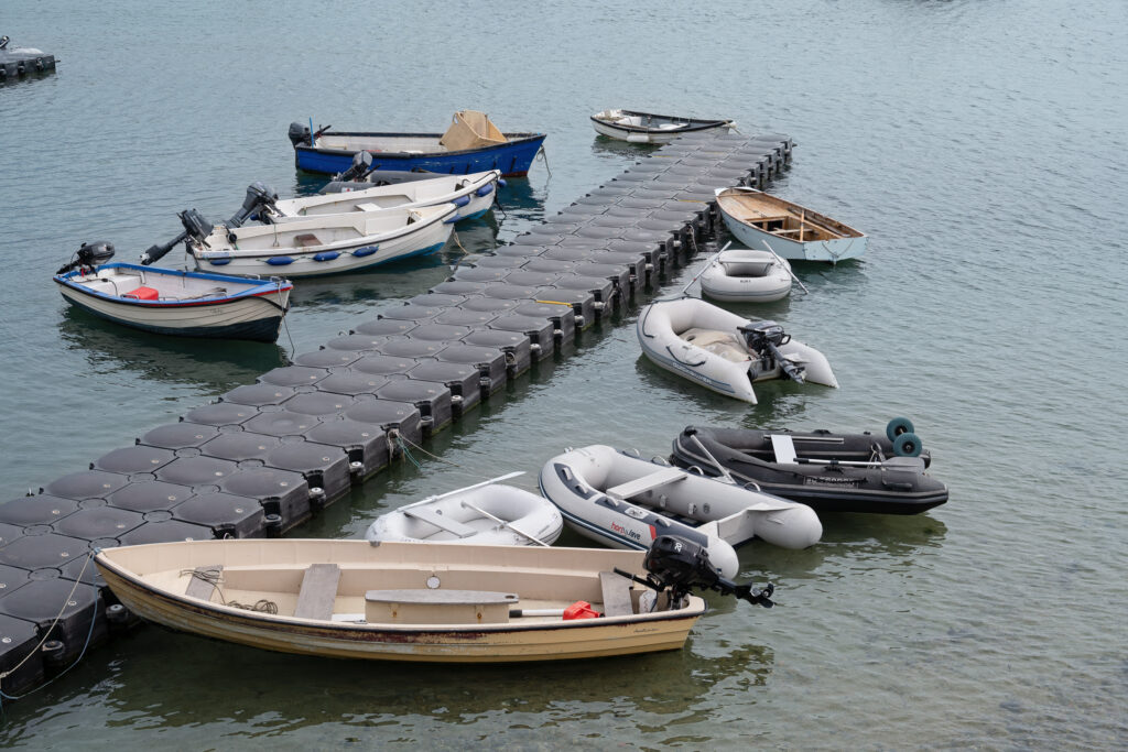 Small boats and dinghies moored around a floating dock in calm water in the Isles of Scilly, England.