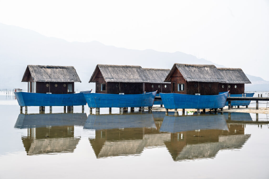 Thatched guest houses on blue stilts reflect in calm lagoon water in Vietnam