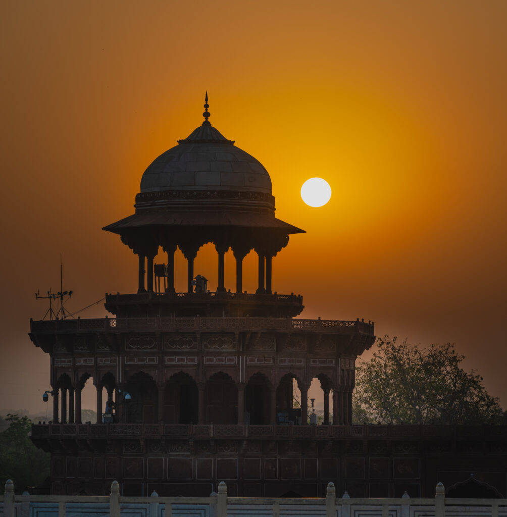 The sun glows in an orange sky beside the dark silhouette of a domed pavilion.