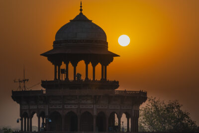 The sun glows in an orange sky beside the dark silhouette of a domed pavilion.
