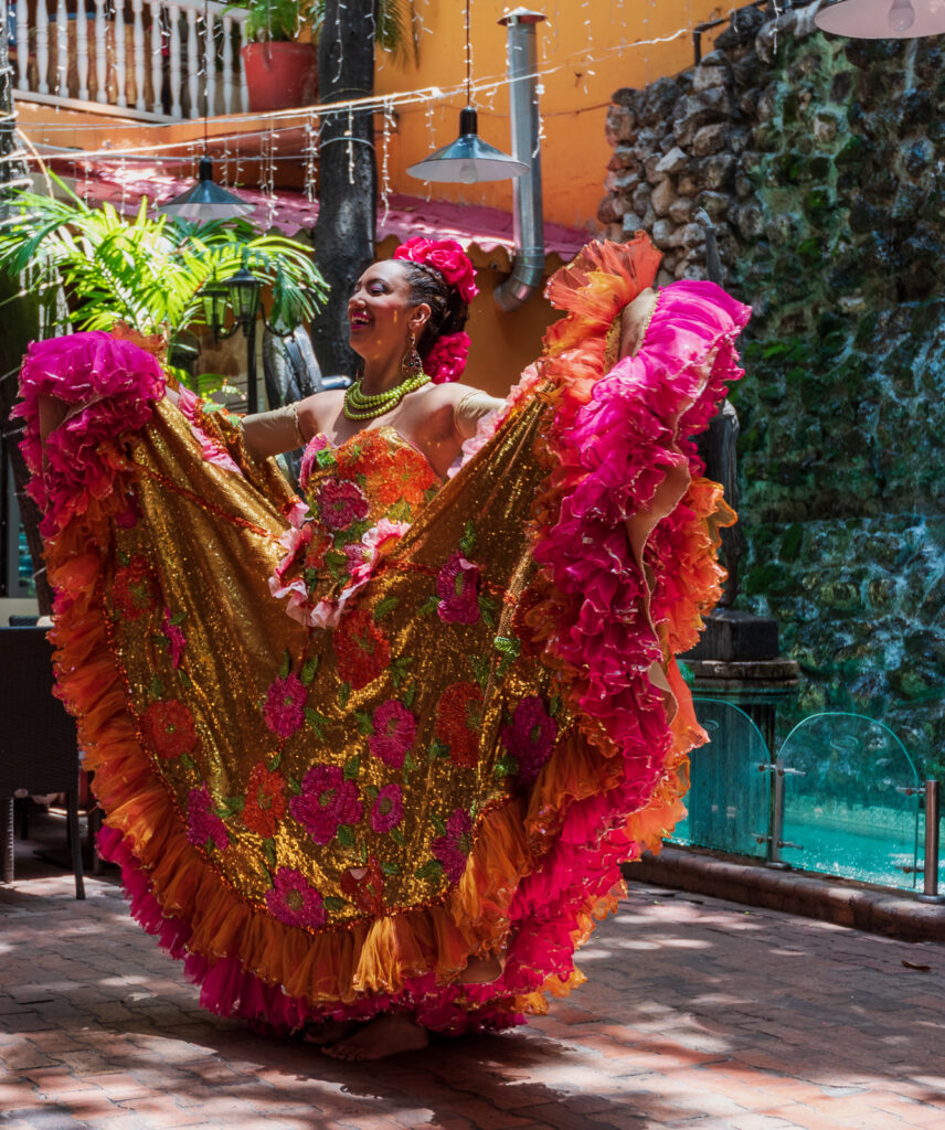 Dancer lifting a red, gold and pink ruffled skirt in a Cartagena courtyard.