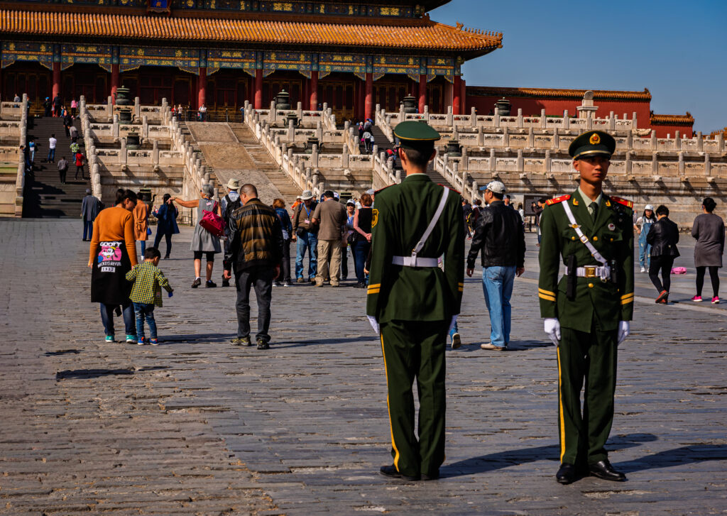 Two uniformed guards stand in a busy palace courtyard in Beijing&rsquo;s Forbidden City.