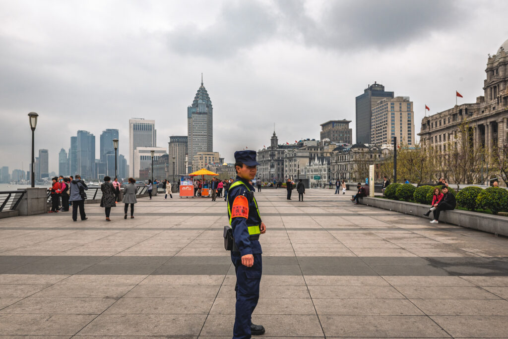 A uniformed officer stands on the Bund promenade with Shanghai&rsquo;s historic waterfront buildings behind.