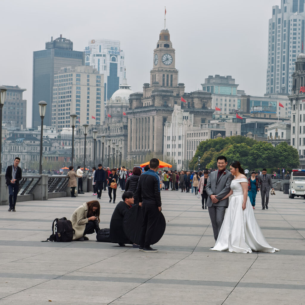 A couple in formal attire poses for a photo session on the Bund promenade in Shanghai, China.