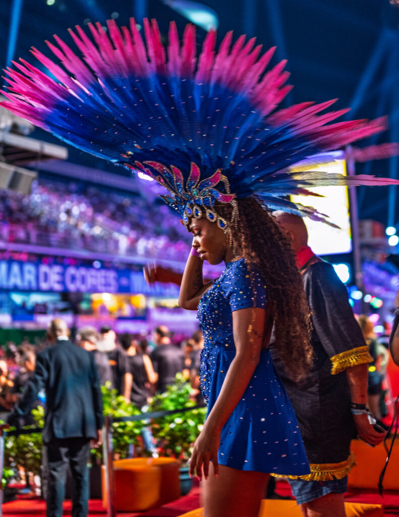 A Carnival performer in Rio de Janeiro wears a blue costume and an expansive blue and pink feathered headdress.