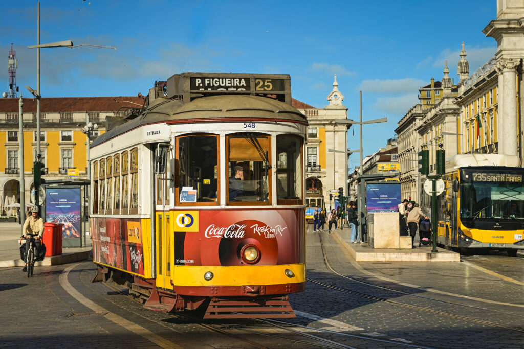 Historic yellow and red Lisbon Tram 25 traveling through Pra&ccedil;a do Com&eacute;rcio under a blue sky in central Lisbon, Portugal.